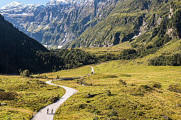 Zwei Radfahrer radeln in trauhafter Bergkulisse und bei bestem Wetter in ein Tal des Nationalparks Hohe Tauern