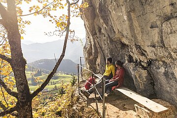 Zwei Personen sitzen auf einer Bank vor einem Felsen