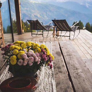 Blumenstrauß auf einem Holztisch, im Hintergrund zwei Liegestühle mit Bergblick