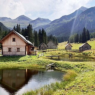idyllische Almhütten mit Holzfassade und kleinen Teichen inmitten einer grünen Berglandschaft