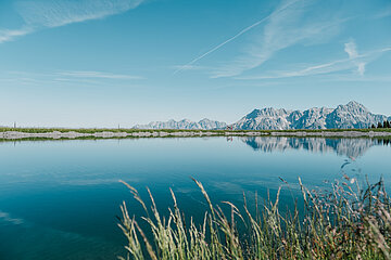 Berggipfel spiegeln sich in einem See, im Vordergrund eine Wiese