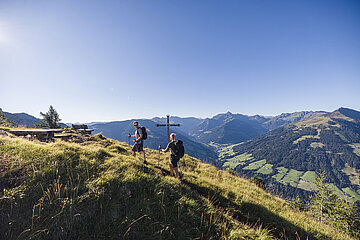 Zwei Wanderer erklimmen ein Gipfelkreuz