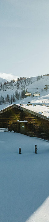 Holzhütte direkt an der Skipiste bei Sonnenschein mit Sessellift gleich nebenan.